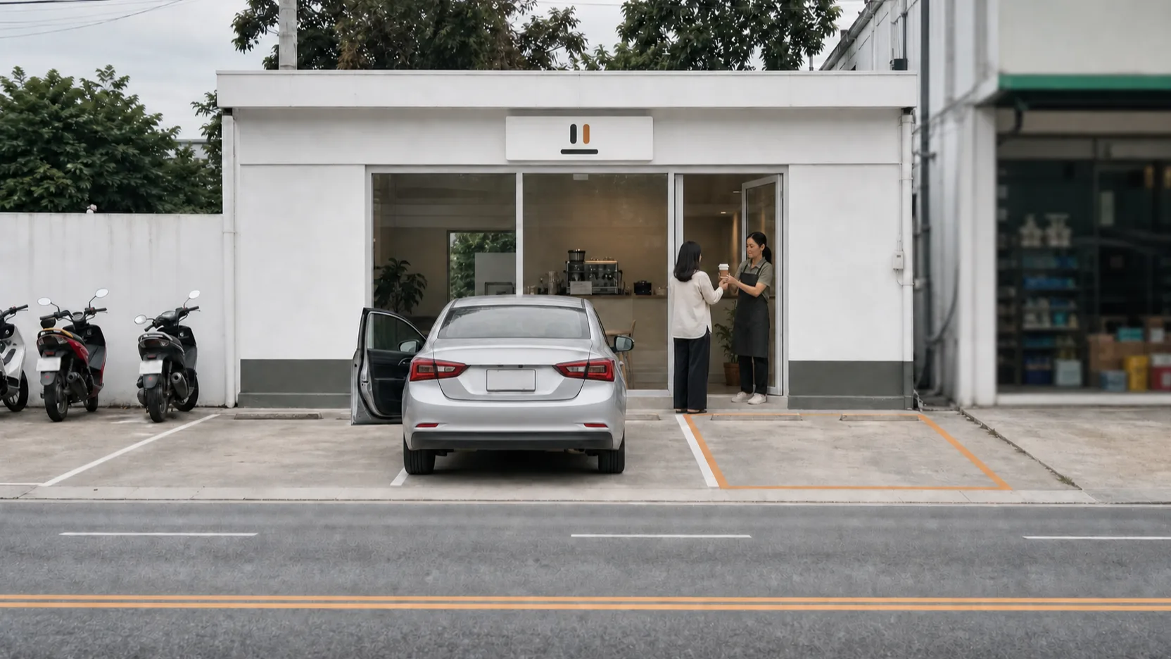 A silver sedan with its driver door open in front of a small white roadside coffee shop, Prae standing in the glass doorway handing a paper cup to a customer whose back is to the camera, motorbikes parked along the left wall