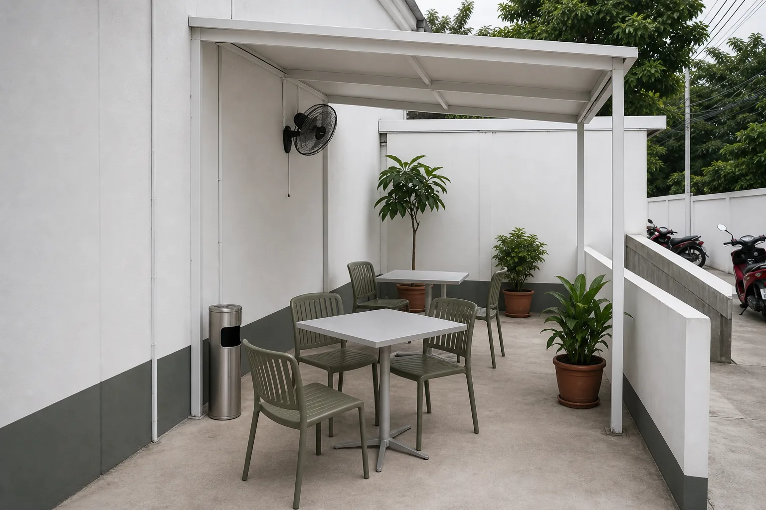 The semi-open side area with two small tables, weatherproof chairs, a standing ashtray and a wall fan — and a clean floor